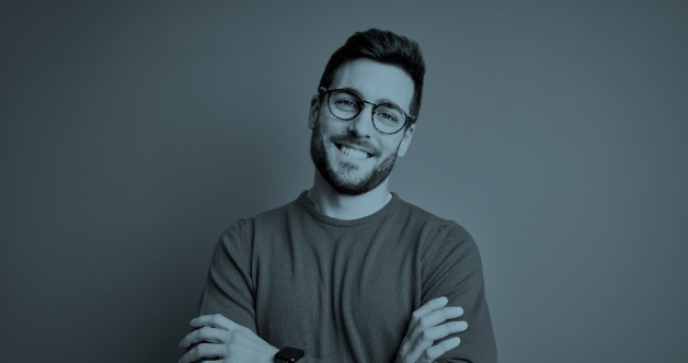 Hombre joven con barba y gafas alegre cruzando los brazos